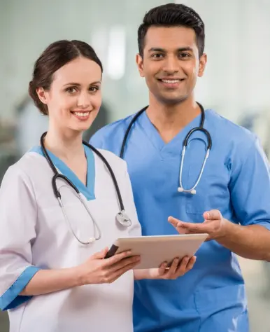 A smiling female nurse in white scrubs and a male nurse in blue scrubs stand together