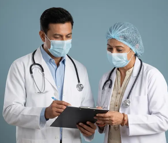 An male doctor and a female colleague wearing a surgical cap and mask review patient notes.