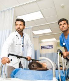 Two male healthcare workers in a hospital emergency unit quickly wheel a patient.